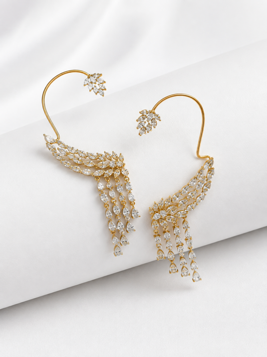 A pair of gold-toned hoop earrings with cascading crystal clusters and small matching crystal studs, displayed on a white draped fabric background.