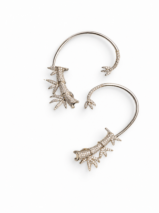 A pair of silver-toned ear cuffs decorated with detailed, textured coral-like motifs paved with small clear rhinestones, shown on a plain white background.